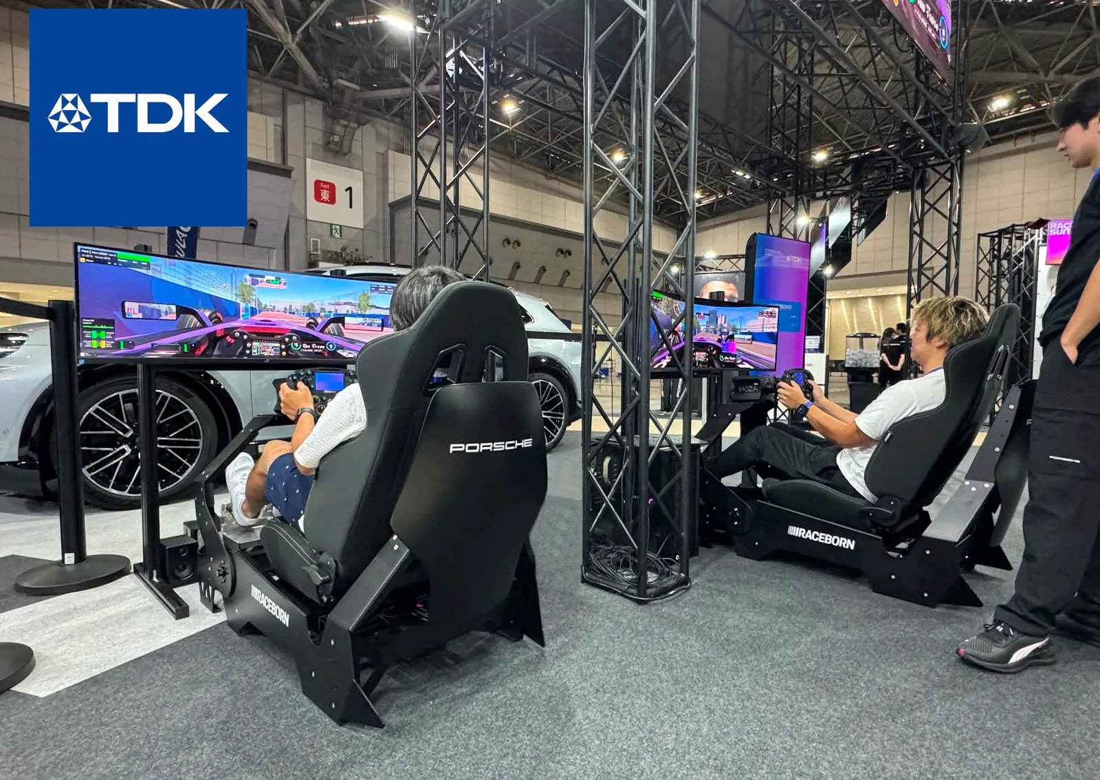 Racing simulators on the Excape stand at a TDK exhibition, with visitors driving and watching