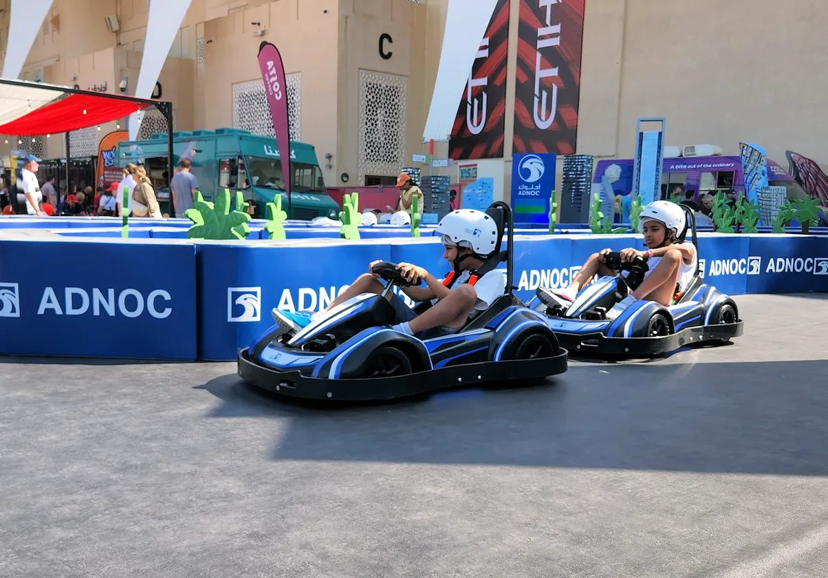 Two children racing electric karts at an ADNOC activation at the Abu Dhabi Grand Prix